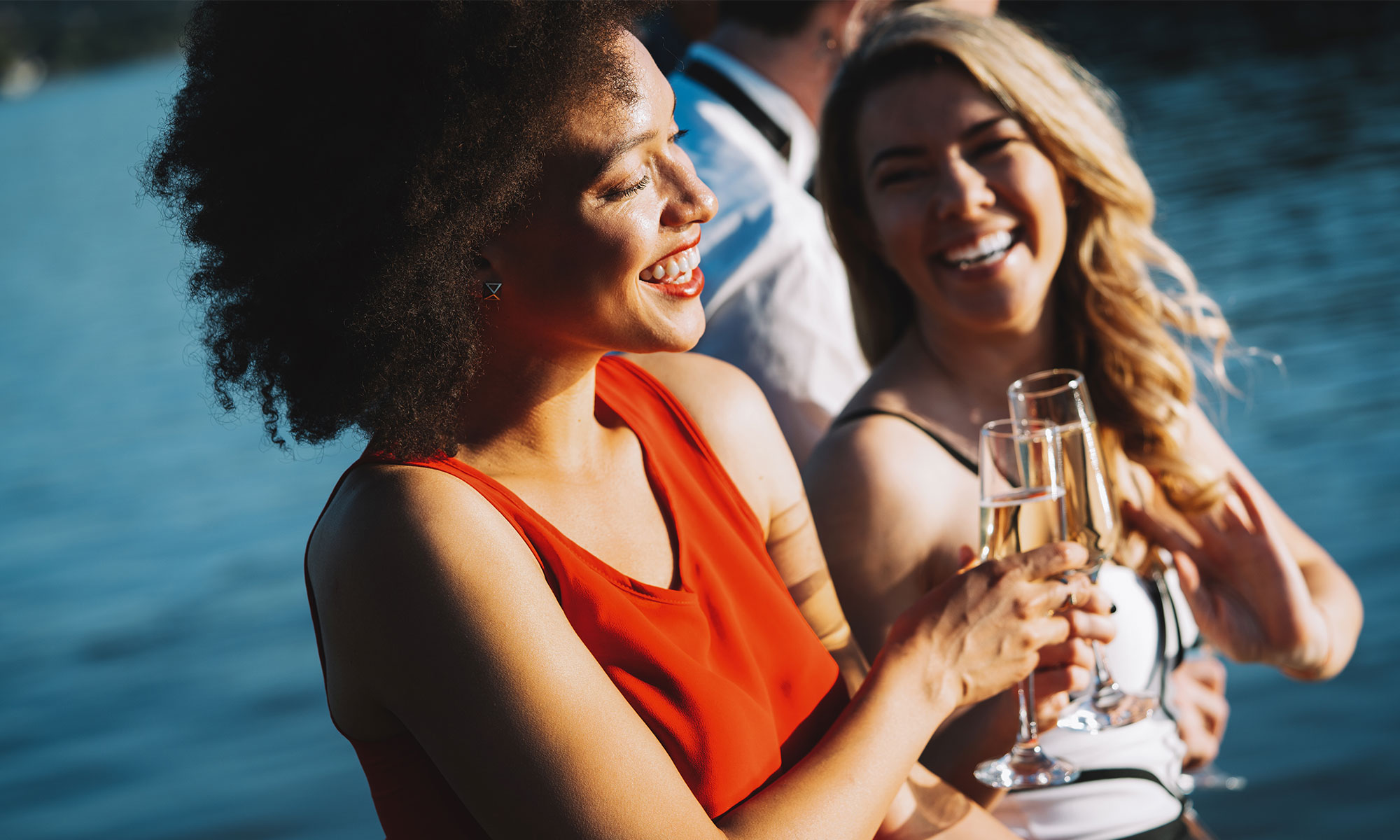 2 women laugh and clink glasses on the waterfront
